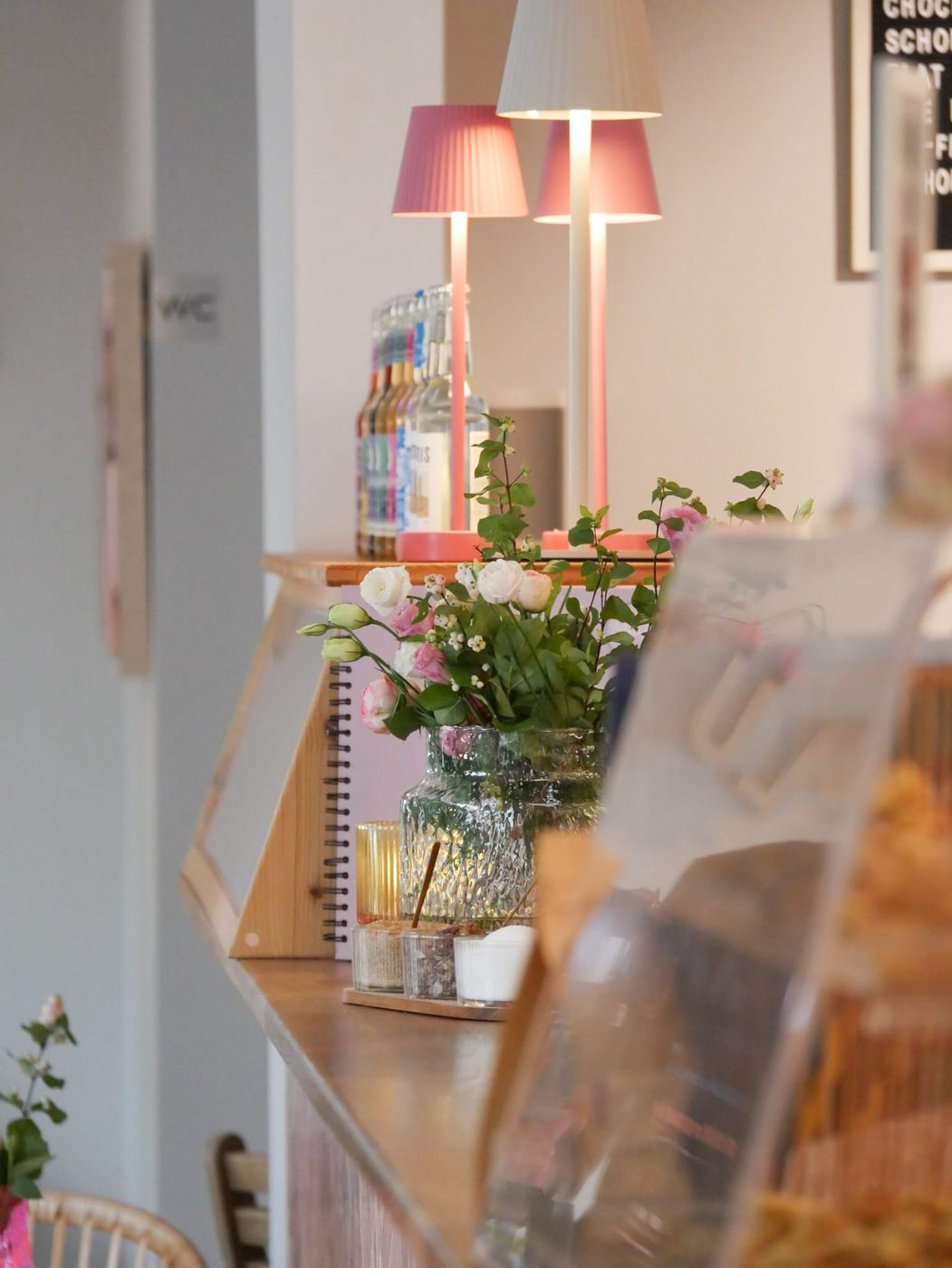 Rosa Lampen, Getränkekarte und frische Blumen am Tresen