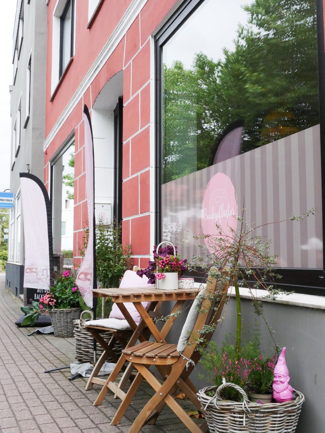 Eingang des Cafés Backgeflüster mit Tisch, Stühlen und Blumen